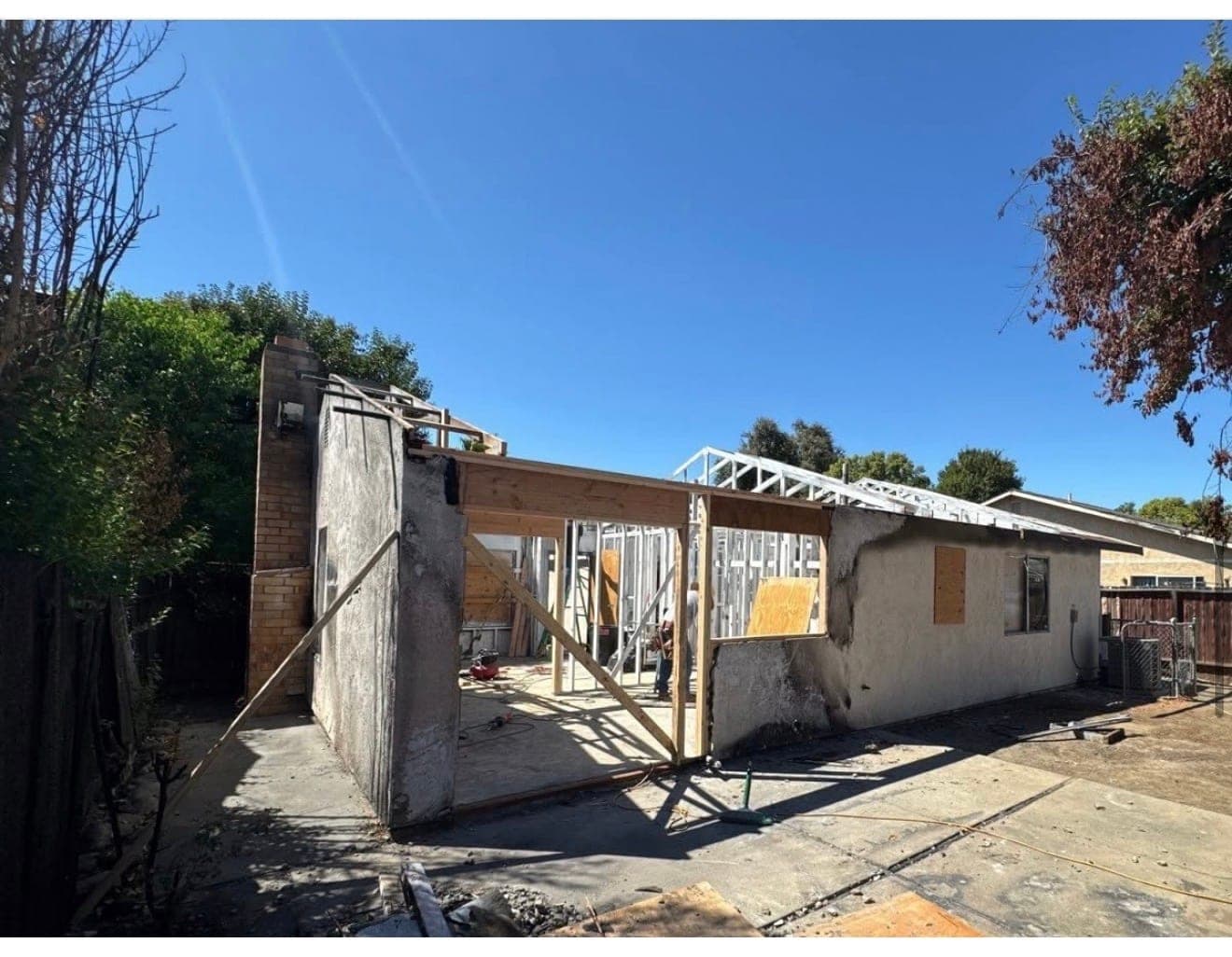 A fire-damaged single-family house being reframed by BEK Construction, with new roof trusses set against a clear sky